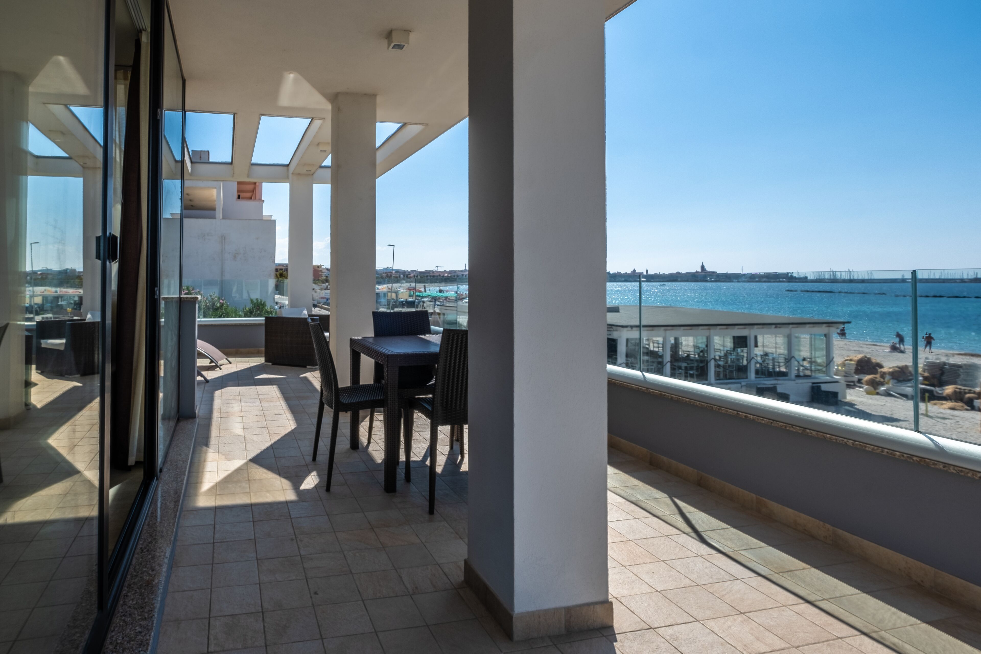 A balcony with a table and chairs, overlooking a beach and water.
