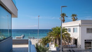 A beach view from a balcony with a clear sky, palm trees, and a restaurant named "Cucina Gour." - Residence Picalè (Alghero)