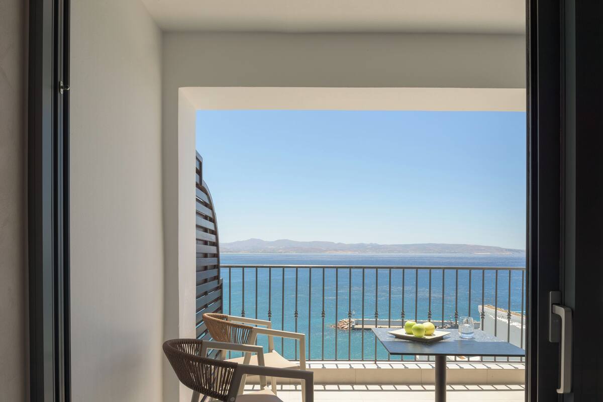 A balcony with a table, chairs, and a view of the sea.