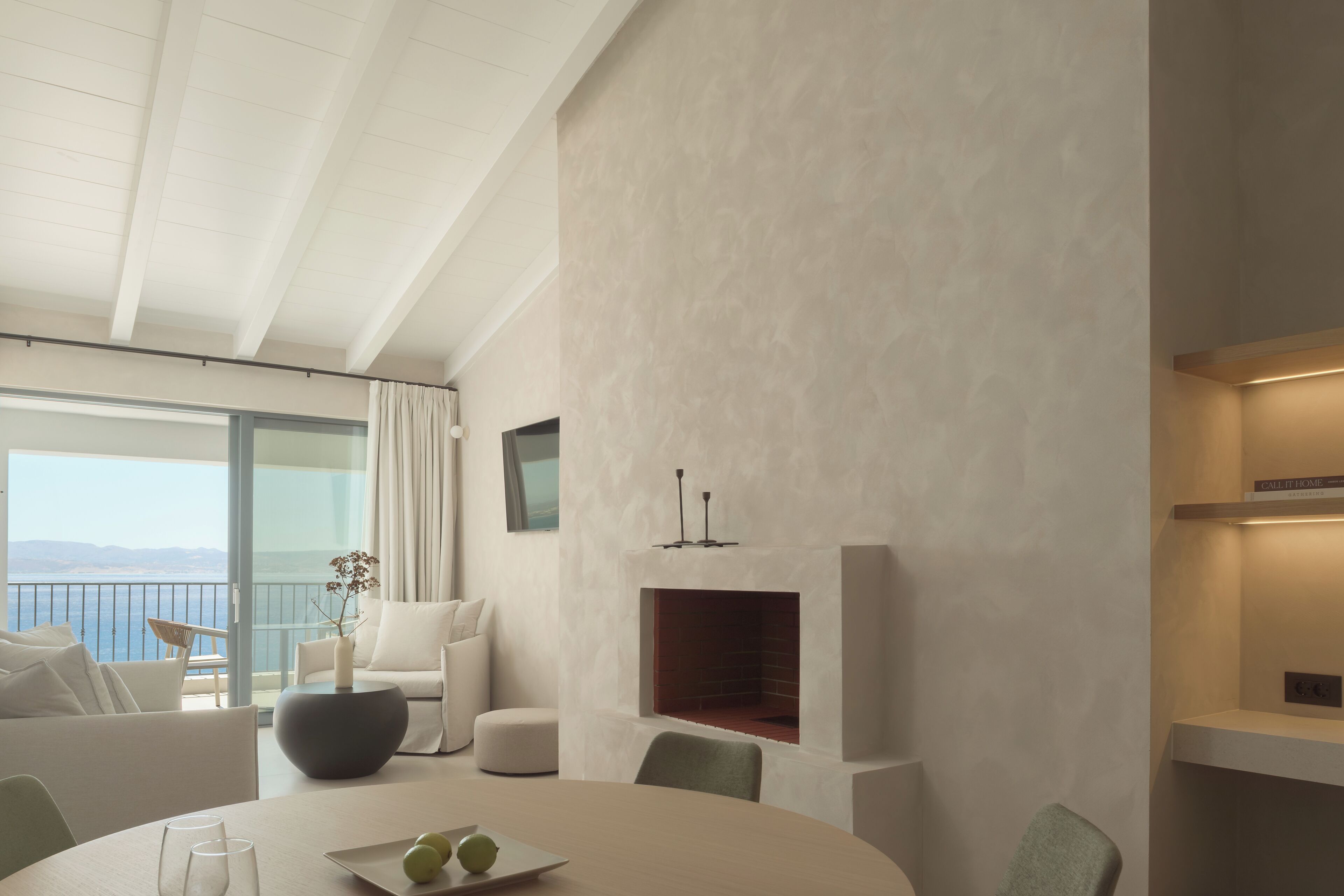 A modern living room with a fireplace, a dining table, and a view of the sea.
