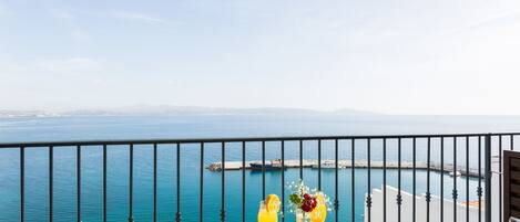 A balcony with a table set for breakfast overlooking a coastal view.