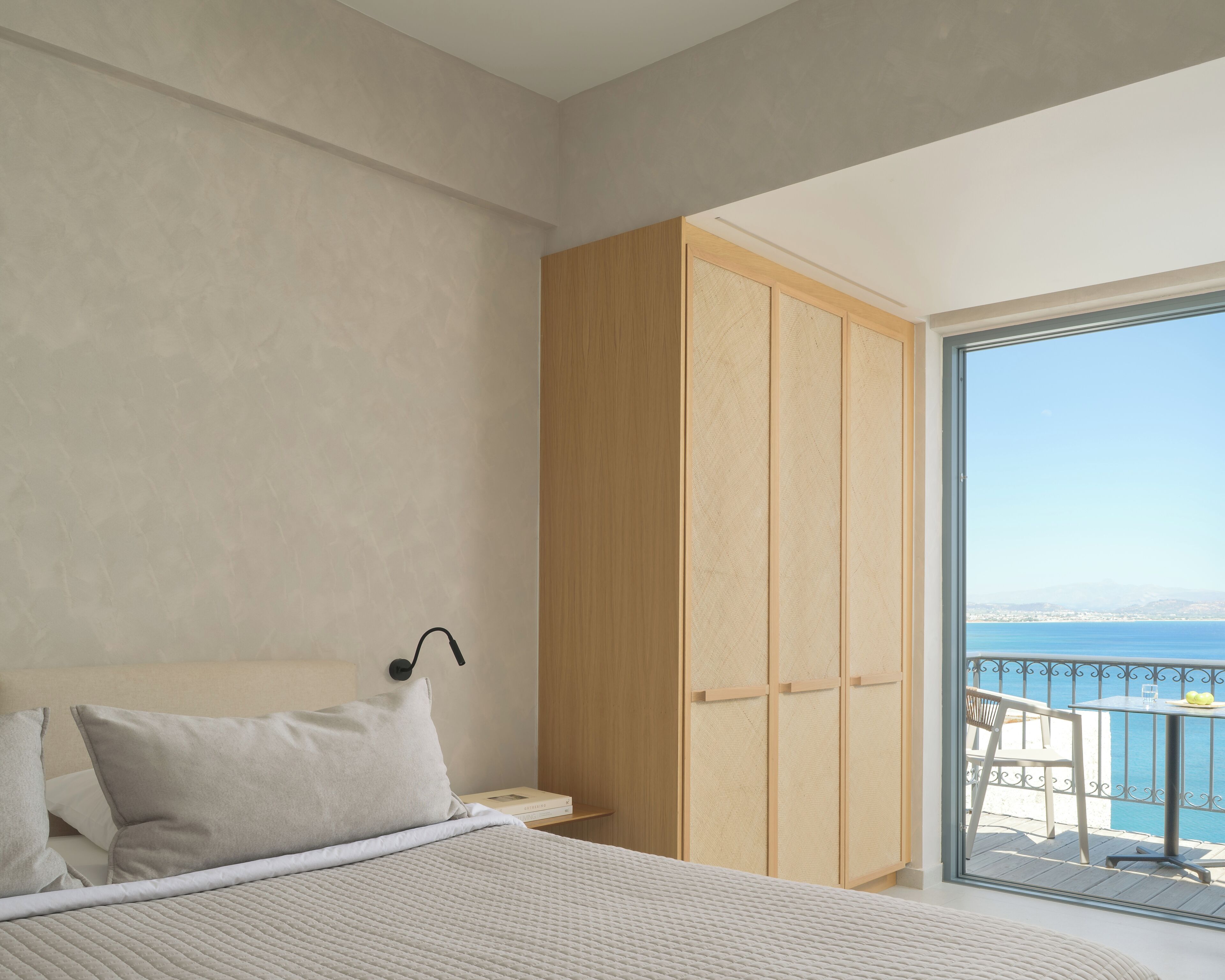 Un dormitorio con cama, un armario de madera y un balcón con vistas al mar.