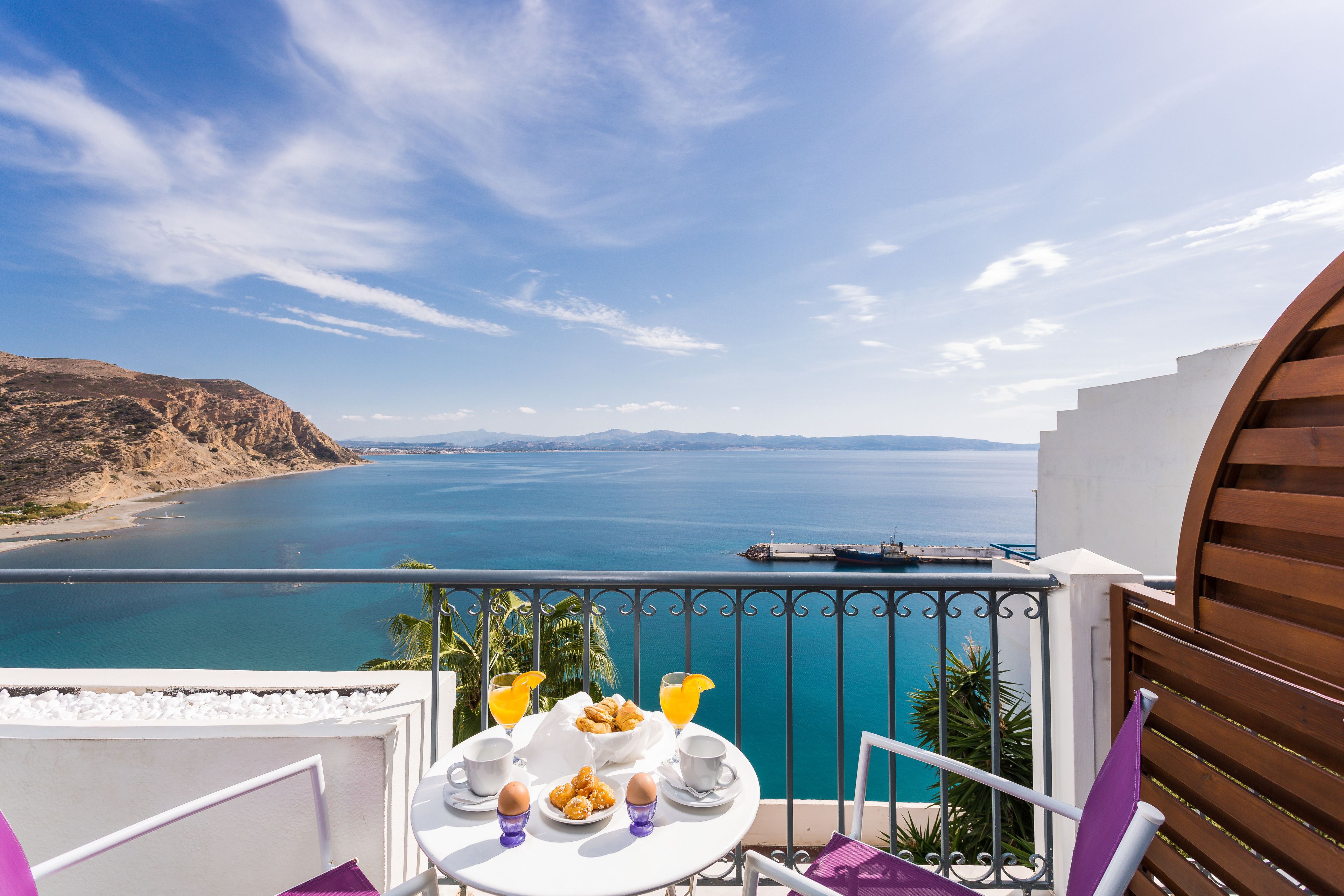 A balcony with a table set for breakfast overlooking a coastal view.