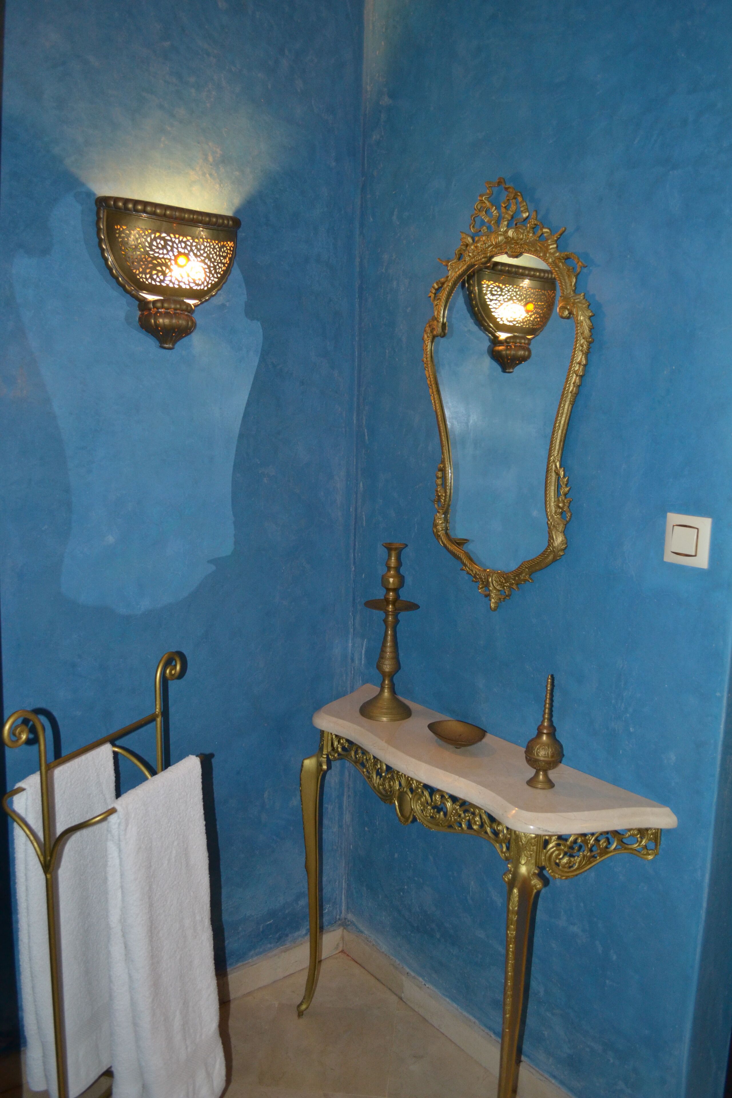 A bathroom with a blue wall, a white marble sink, and a gold-framed mirror.