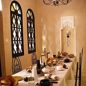 A dining table set with various dishes, a chandelier, and decorative window grills.