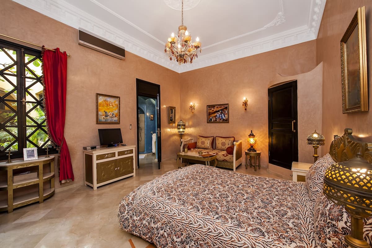 A bedroom with a large bed, a TV, a desk, and a wardrobe.