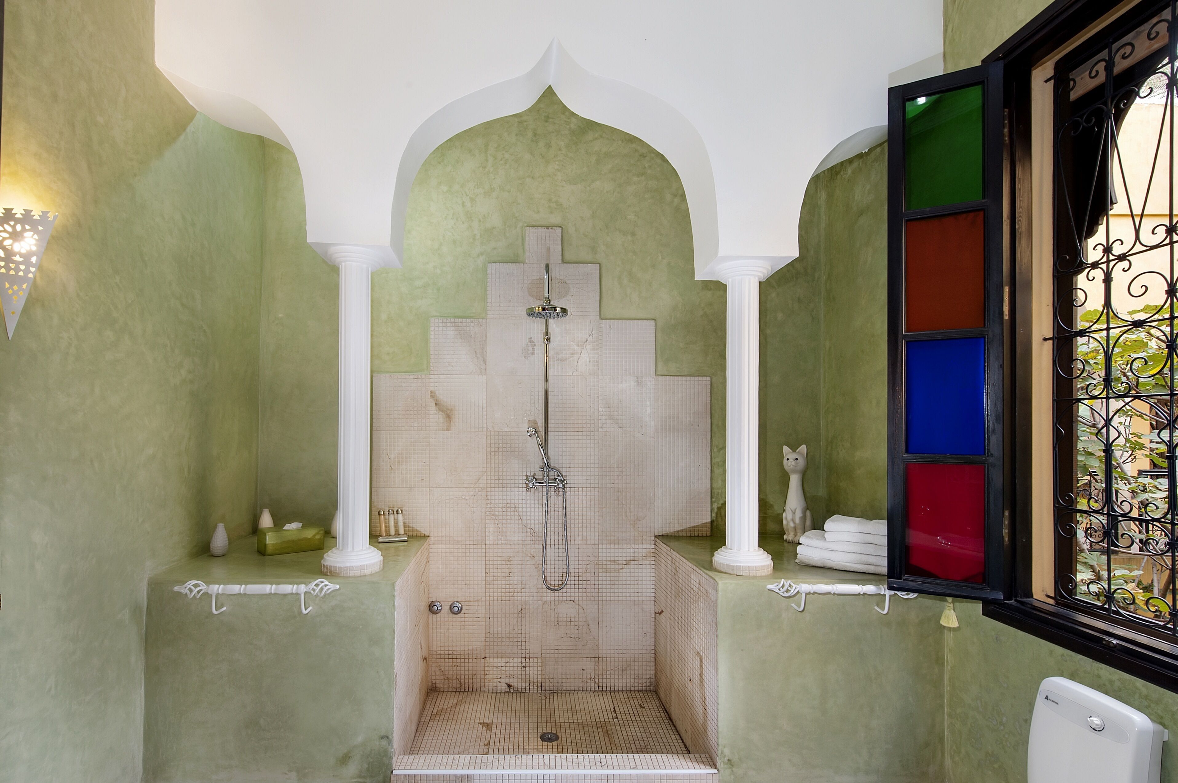 A bathroom with a shower, tiled walls, and a window with colored glass panes.