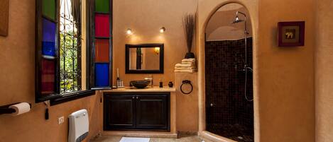 A bathroom with a large mirror, a sink with a bowl, a towel rack, and a shower with a tiled wall.