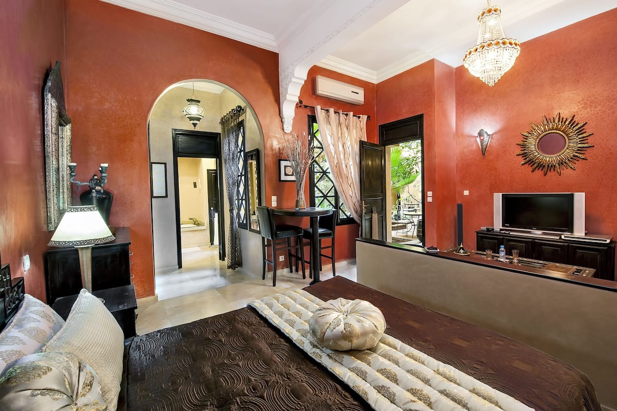 A room with a bed, a TV, a dining area, and a chandelier.