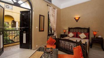 A room with a bed, a table with a book, a balcony with a view, and a wall-mounted light fixture.