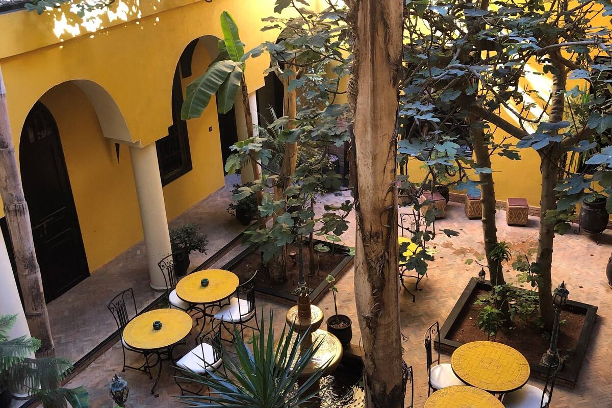 An outdoor patio area with yellow walls, multiple tables and chairs, and potted plants.