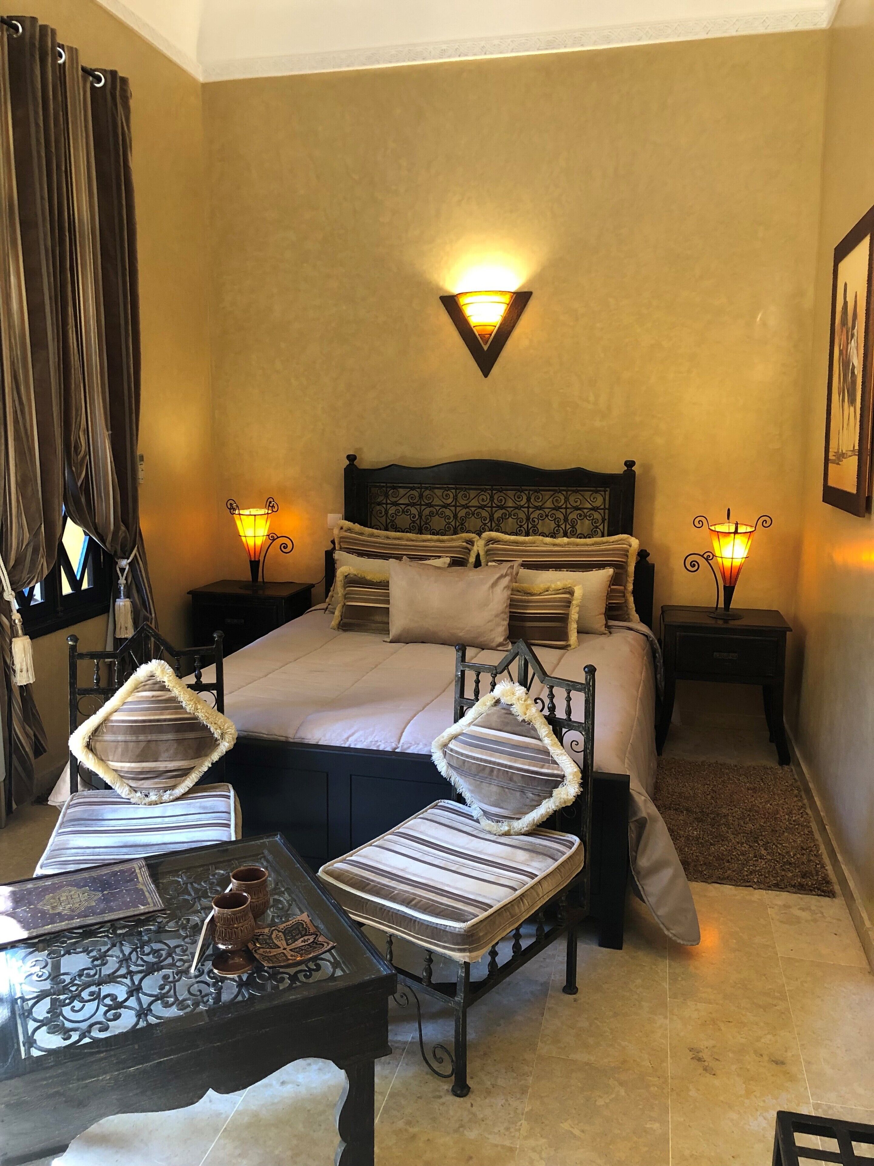 A hotel room with a large bed, two bedside tables with lamps, a small table with decorative items, and a chair with a striped cushion.