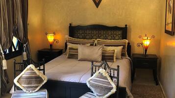 A hotel room with a large bed, two bedside tables with lamps, a small table with decorative items, and a chair with a striped cushion.