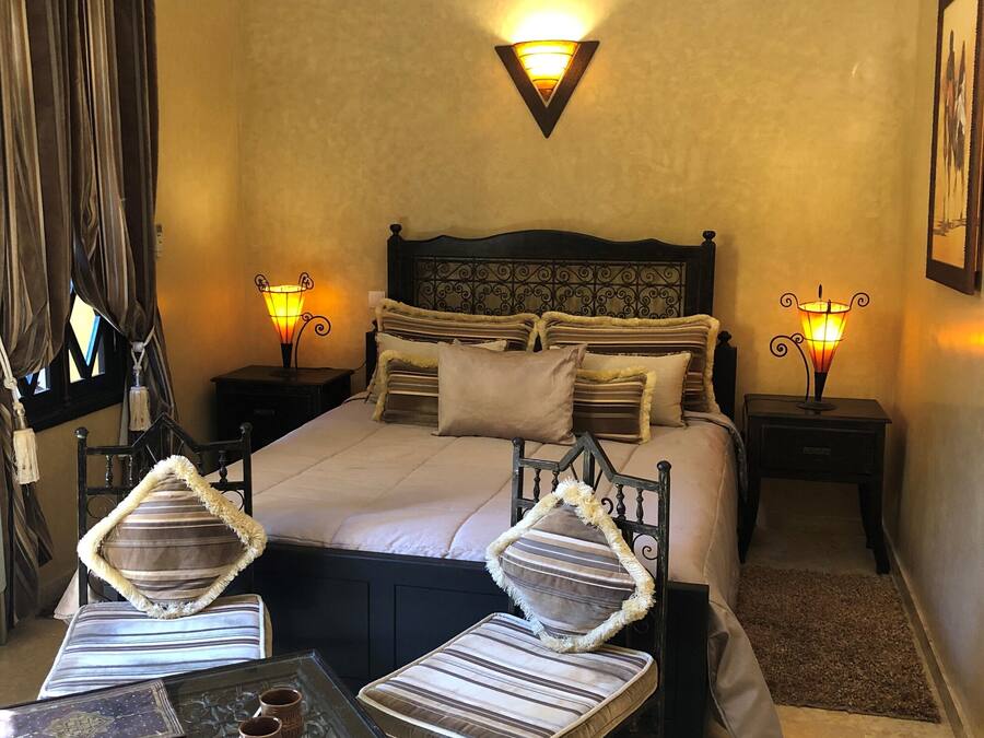 A hotel room with a large bed, two bedside tables with lamps, a small table with decorative items, and a chair with a striped cushion.