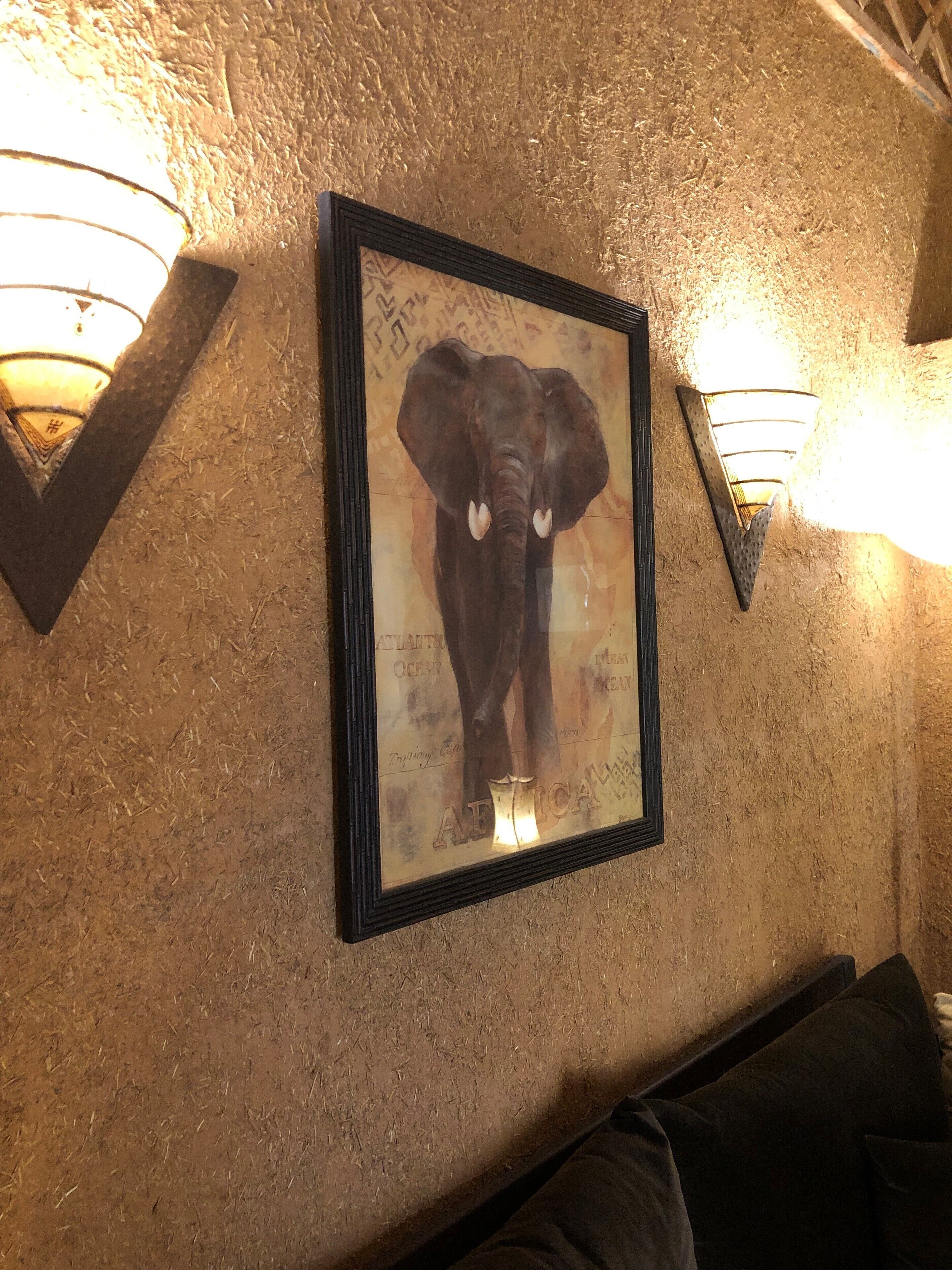 A framed elephant artwork on a textured wall with two wall-mounted lights.