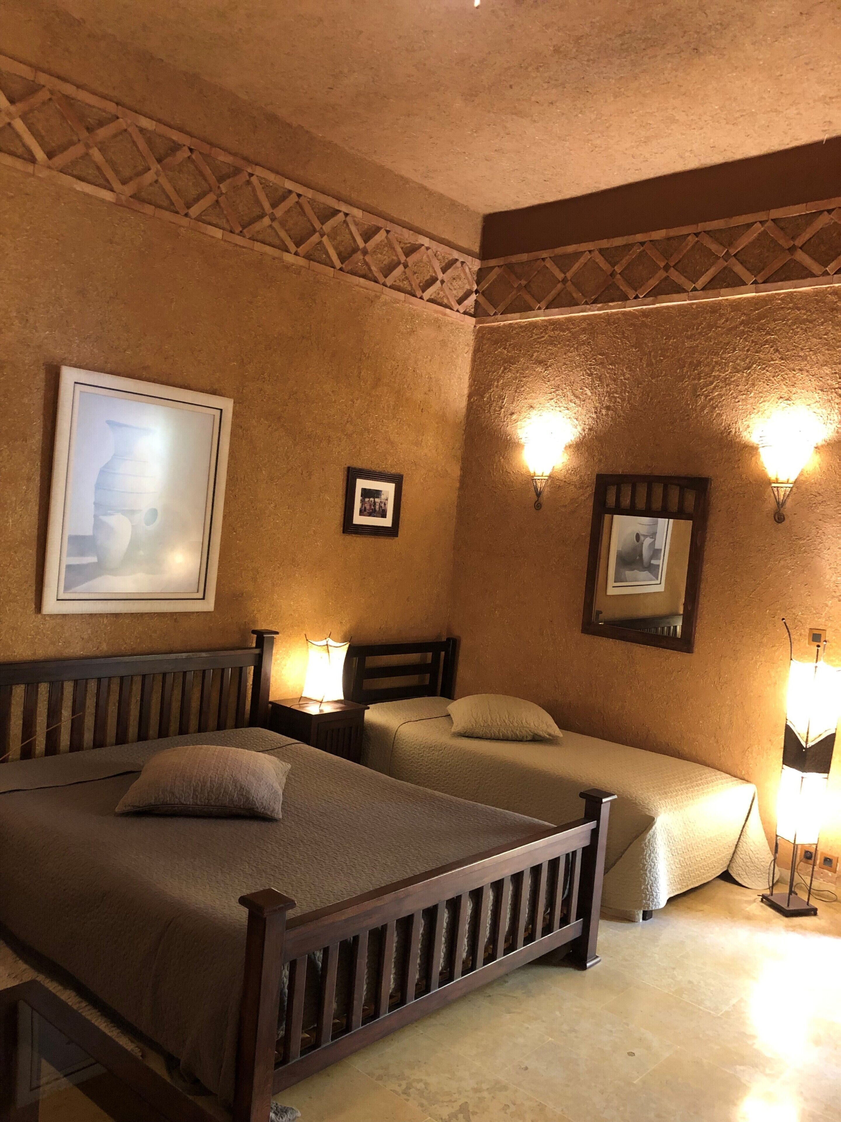 Habitación de hotel con dos camas, cabecero de madera, un cuadro en la pared y luces fijadas a la pared.