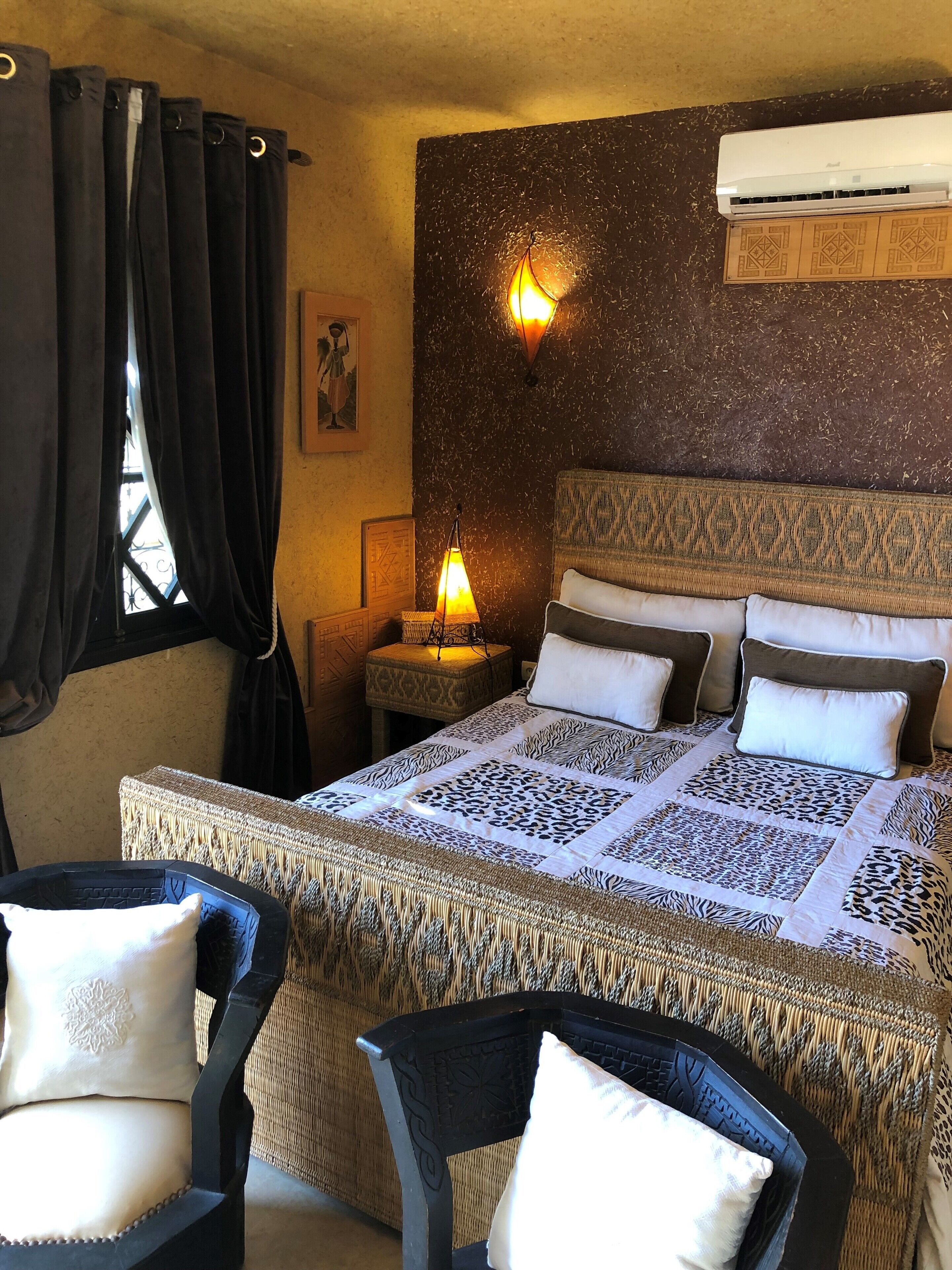 Ein Hotelzimmer mit einem Bett, zwei Sesseln, einem Nachttisch, einer Klimaanlage und einer Wandlampe.