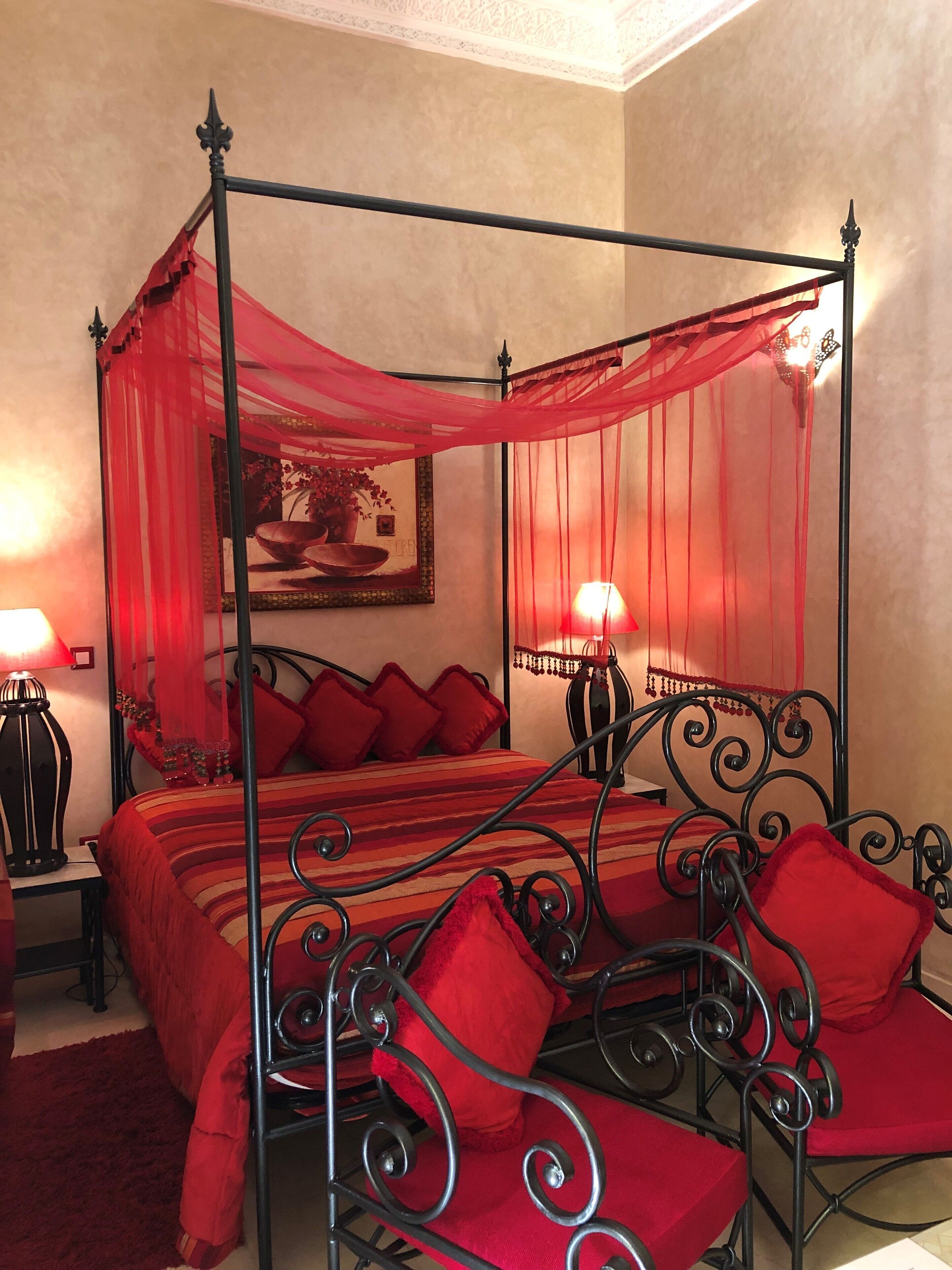 A four-poster canopy bed with red bedding and pillows, two bedside lamps, and a framed picture on the wall.