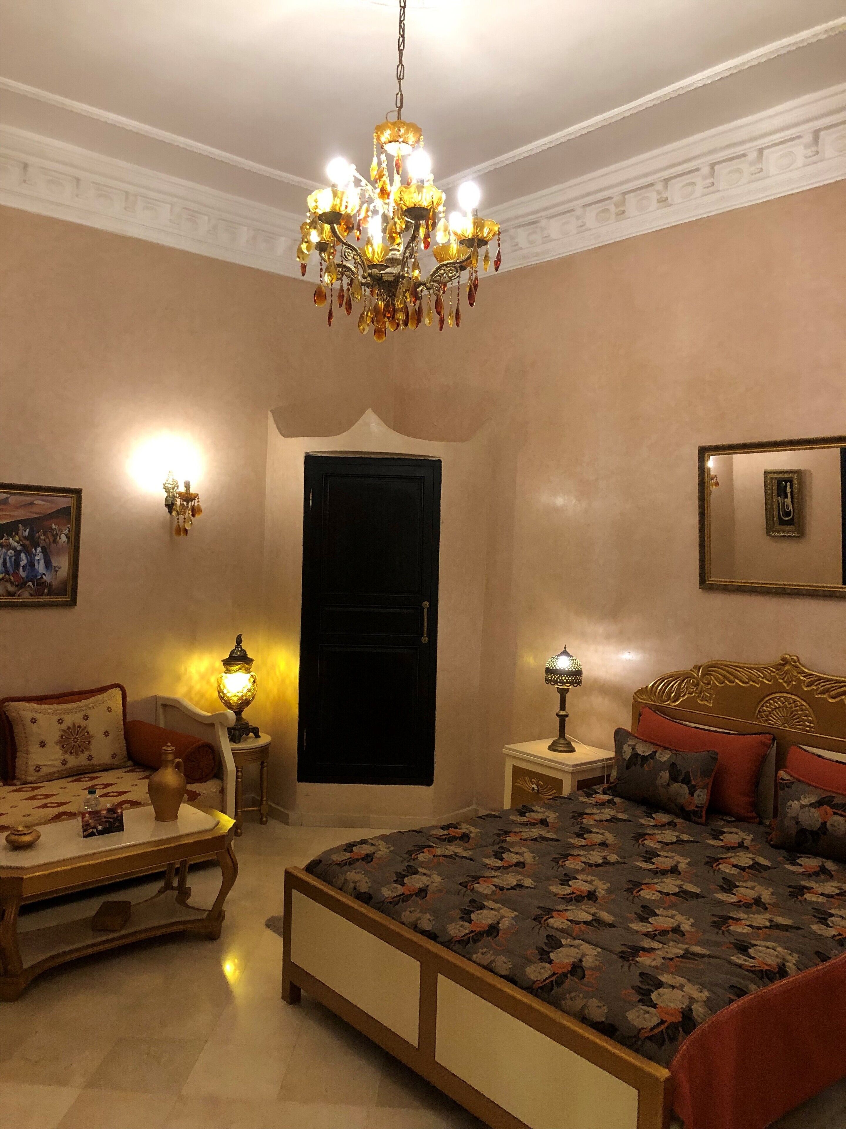 A bedroom with a bed, bedside tables, a chandelier, a wall-mounted picture, and a door.