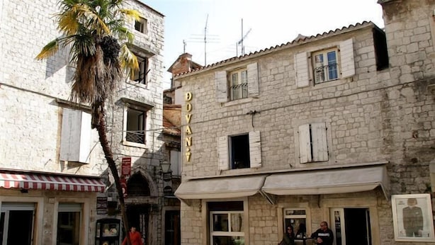 A stone building with a sign reading "DOVAN" and a palm tree in front. - Villa Carrara (Trogir)