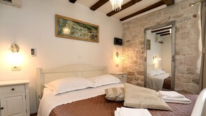 A neatly made bed with white and brown bedding, a painting on the wall, and a stone wall with a mirror reflecting the room. - Villa Carrara (Trogir)