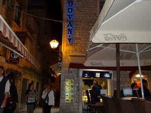 An outdoor dining area with a stone facade, a neon sign, and a Coca-Cola branded umbrella. - Villa Carrara (Trogir)