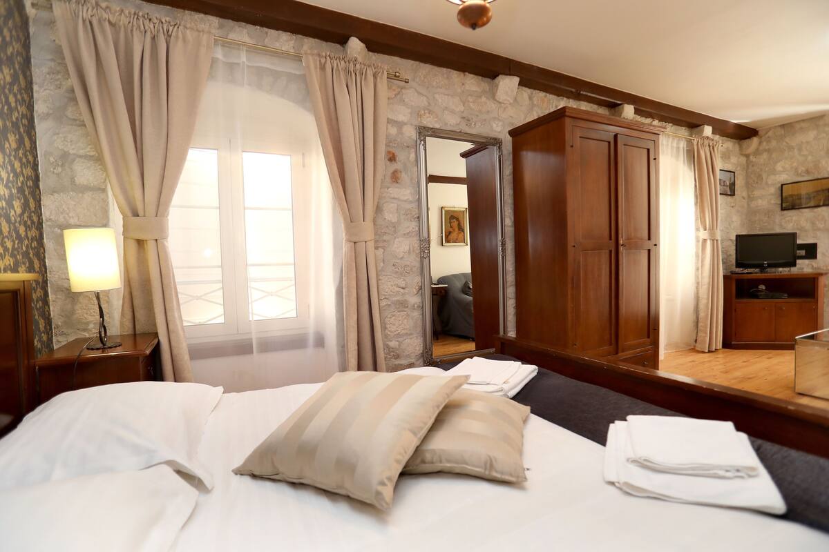 A hotel room with a bed, curtains, a mirror, a TV, and a wooden wardrobe.