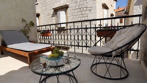 A balcony with a wooden bed, a glass table with a fruit bowl, and a wicker chair. - Villa Carrara (Trogir)