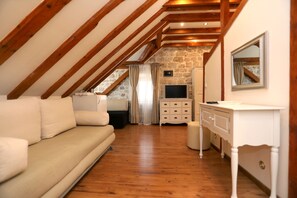 A cozy attic bedroom with a wooden ceiling, a stone wall, a TV, a dresser, and a sofa.