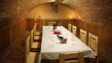 A long dining table set with wine glasses, bottles, and a candle centerpiece in a brick-walled room with wooden benches.