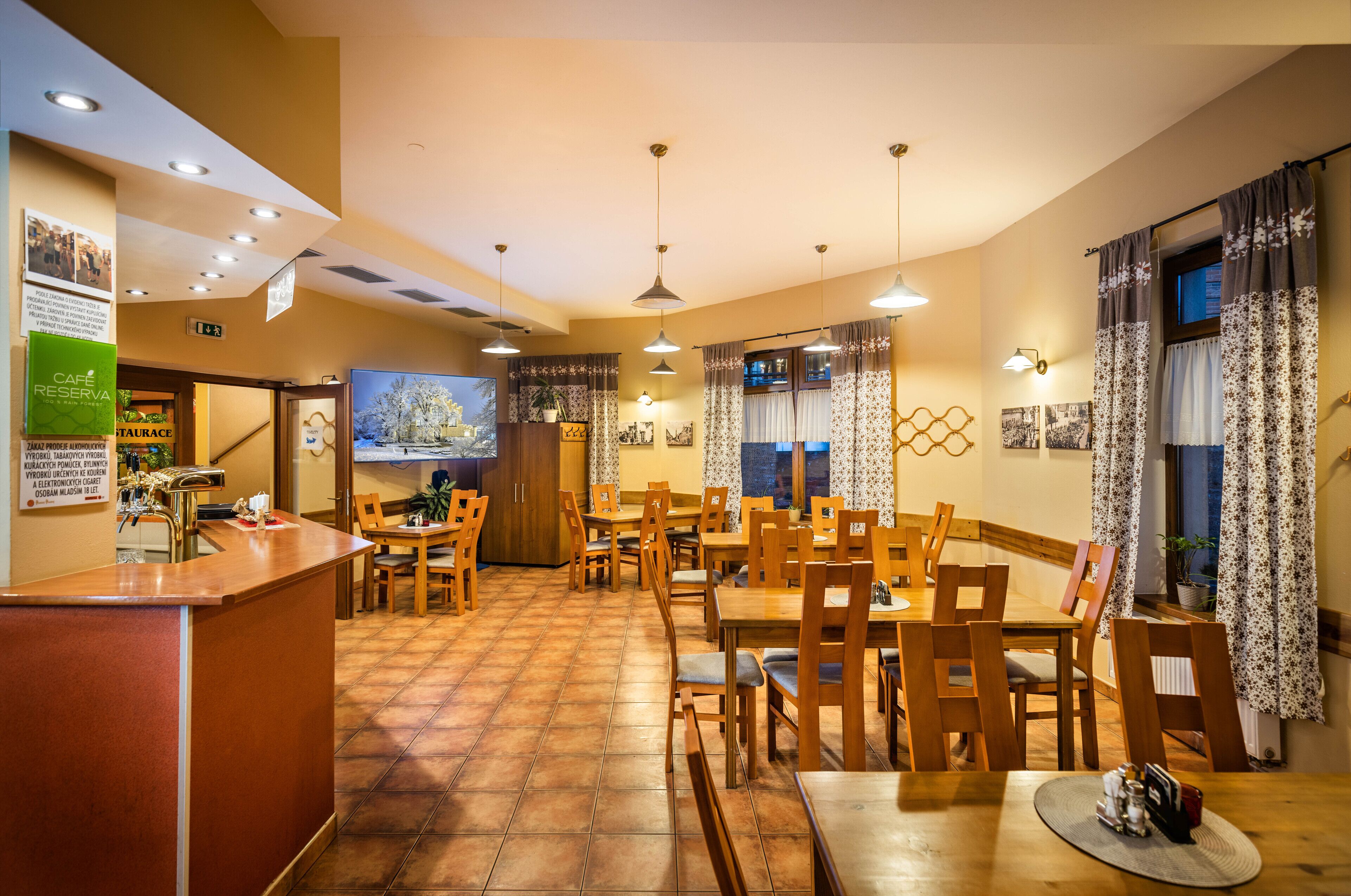 A restaurant with wooden tables and chairs, a counter, and a TV screen.