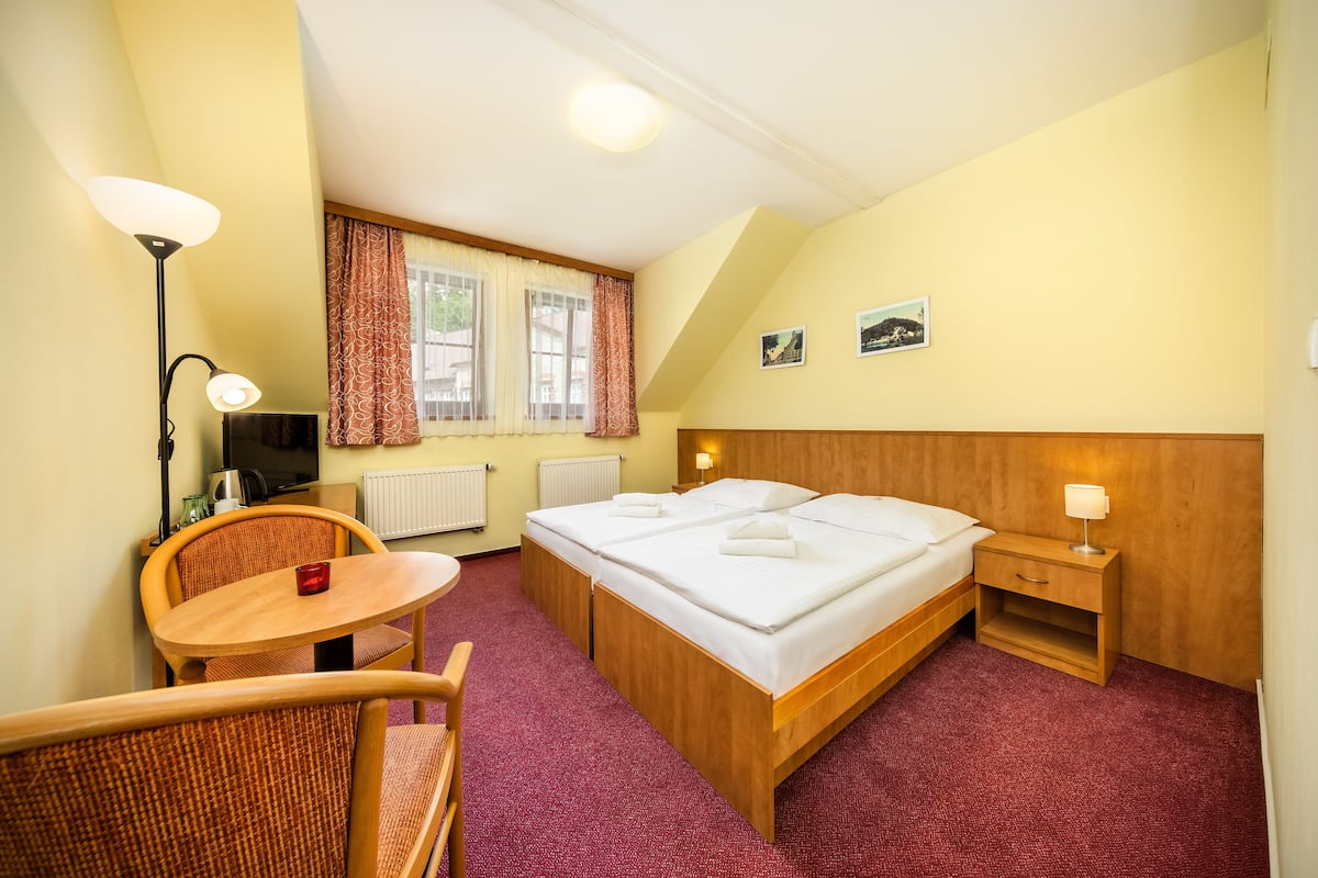 Une chambre d’hôtel avec un grand lit, un petit bureau, une chaise, une lampe et une fenêtre avec des rideaux.