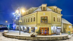 A hotel with a restaurant on the ground floor, featuring a snow-covered outdoor seating area and a stone wall surrounding the property. - Hotel Záviš z Falkenštejna (Hluboka nad Vltavou)