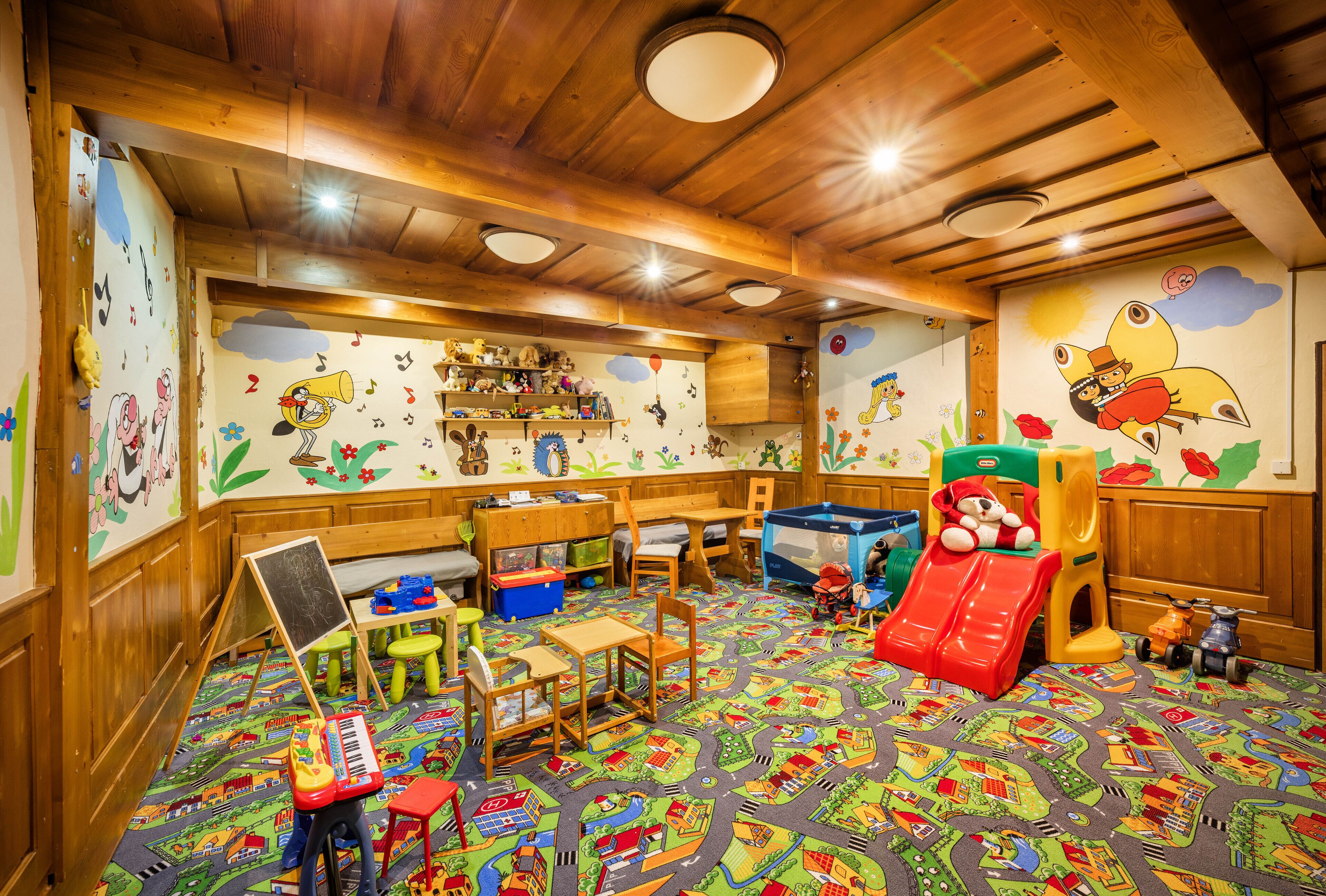 Une salle de jeux pour enfants avec des meubles en bois, un toboggan, des jouets et des décorations murales colorées.