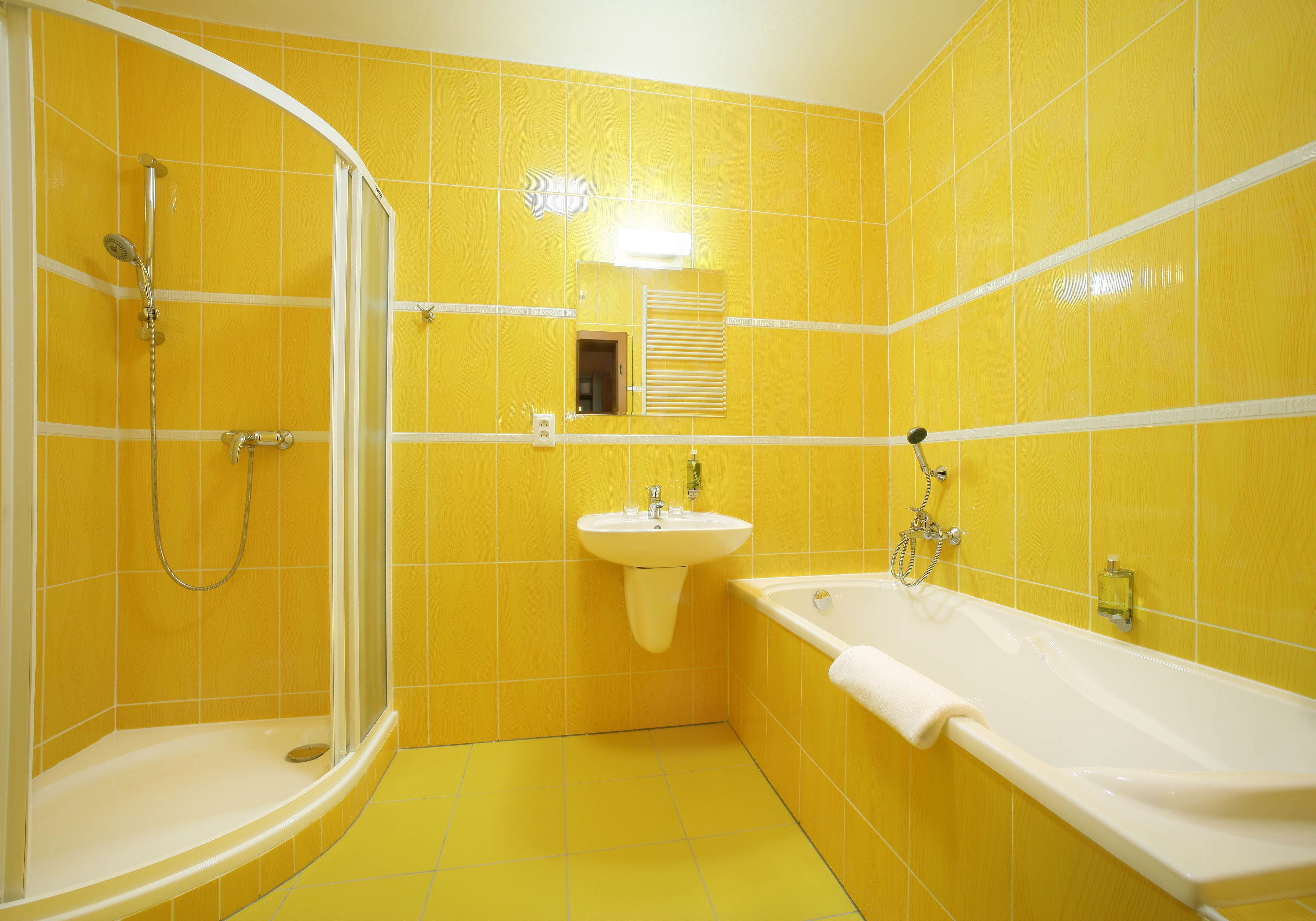 Uma casa de banho com azulejos amarelos, uma pia, uma banheira e um espaço de duche.