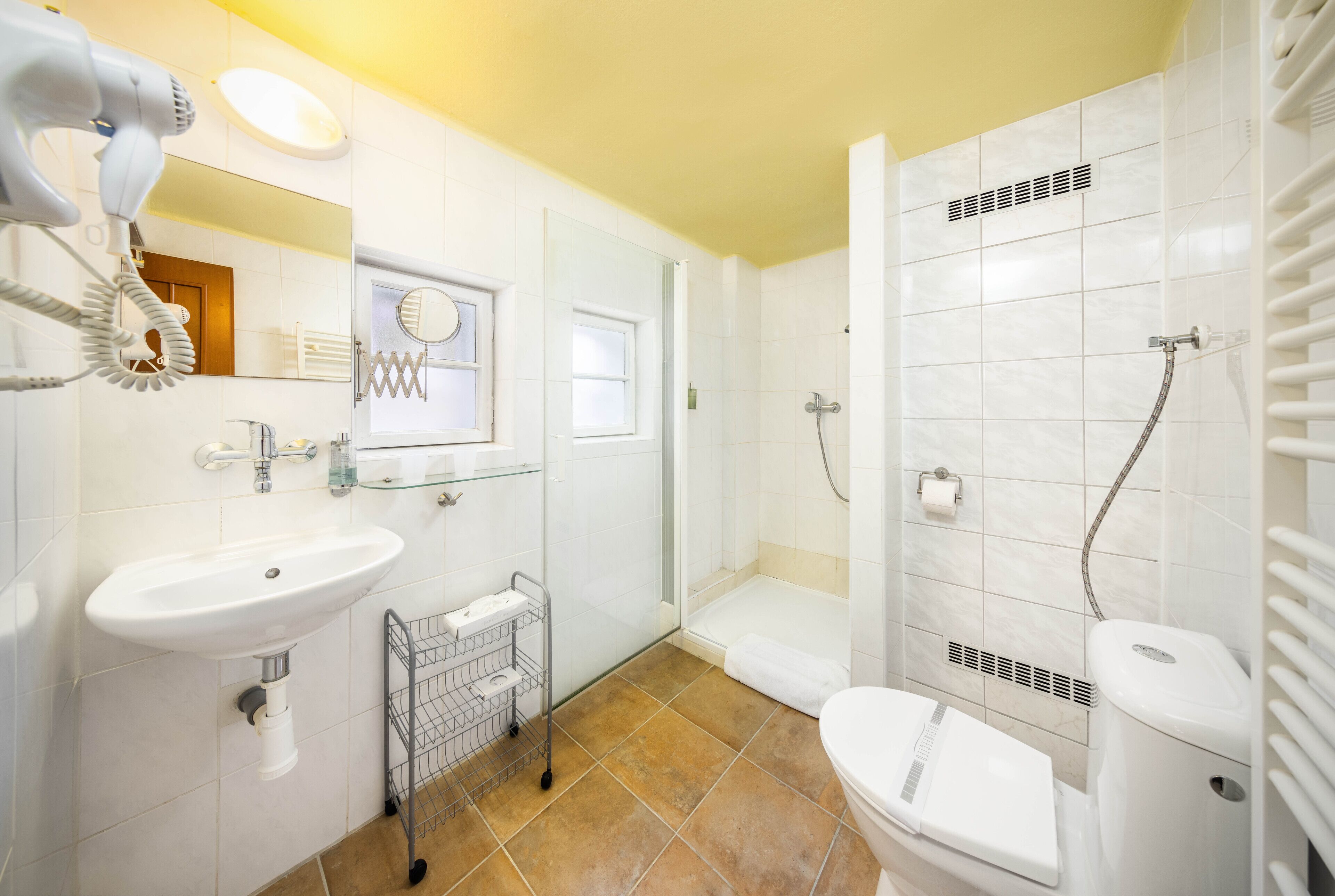 Un baño con lavamanos, espejo, secador de pelo, ducha e inodoro.