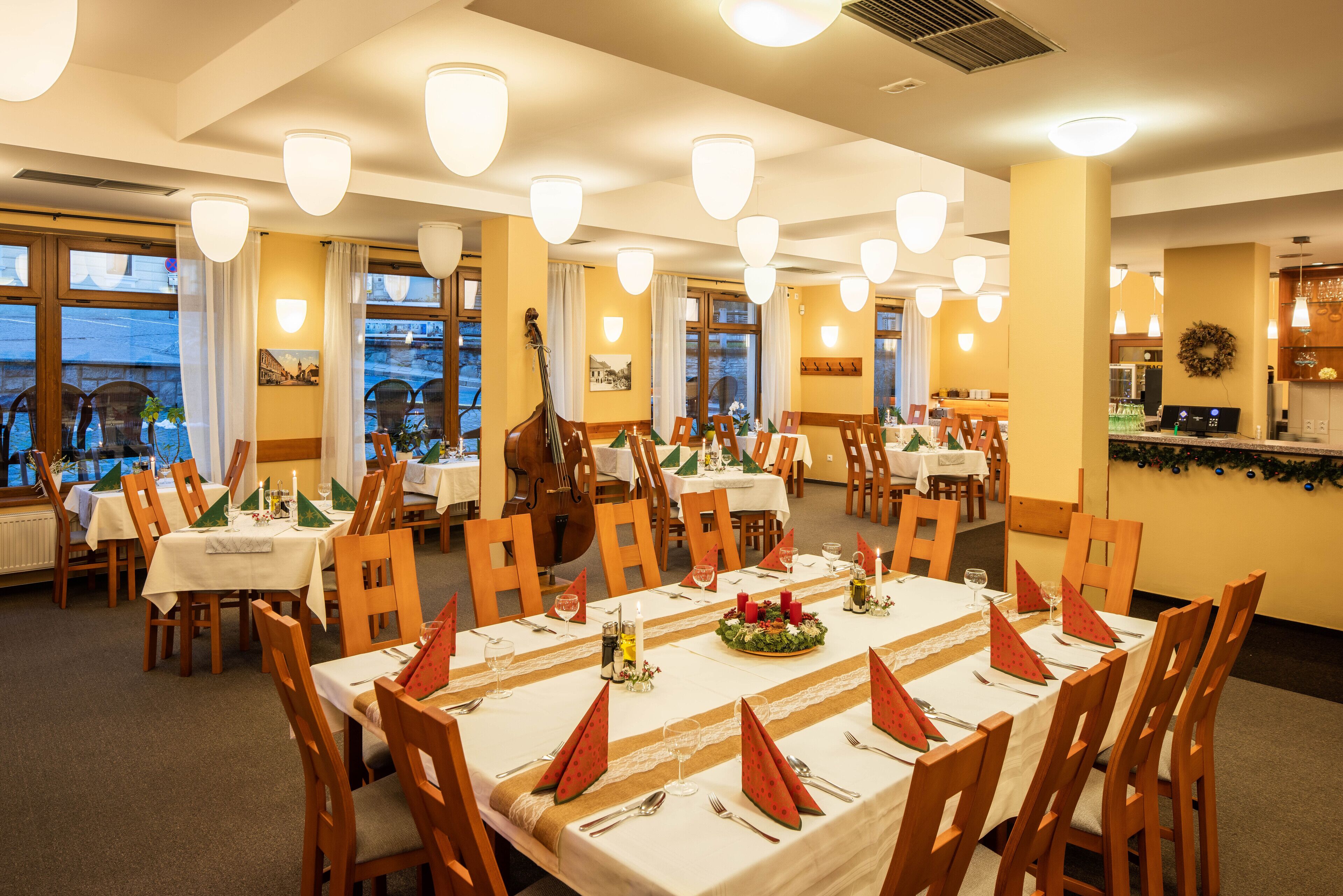A dining area with multiple tables set for a meal, wooden chairs, and a view of the outside through large windows.