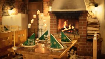 A dining table set with green napkins, wine glasses, and candles, with a brick fireplace in the background.