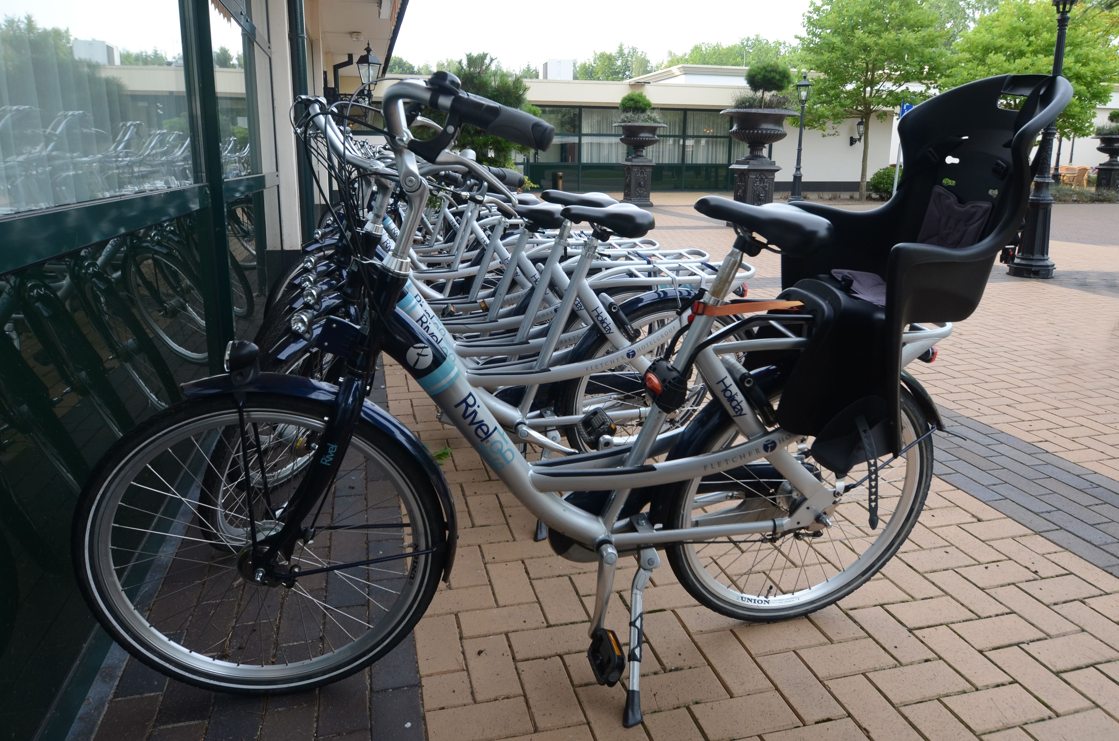 Eine Reihe von Fahrrädern, die vor einem Gebäude mit Pflasterboden abgestellt sind.