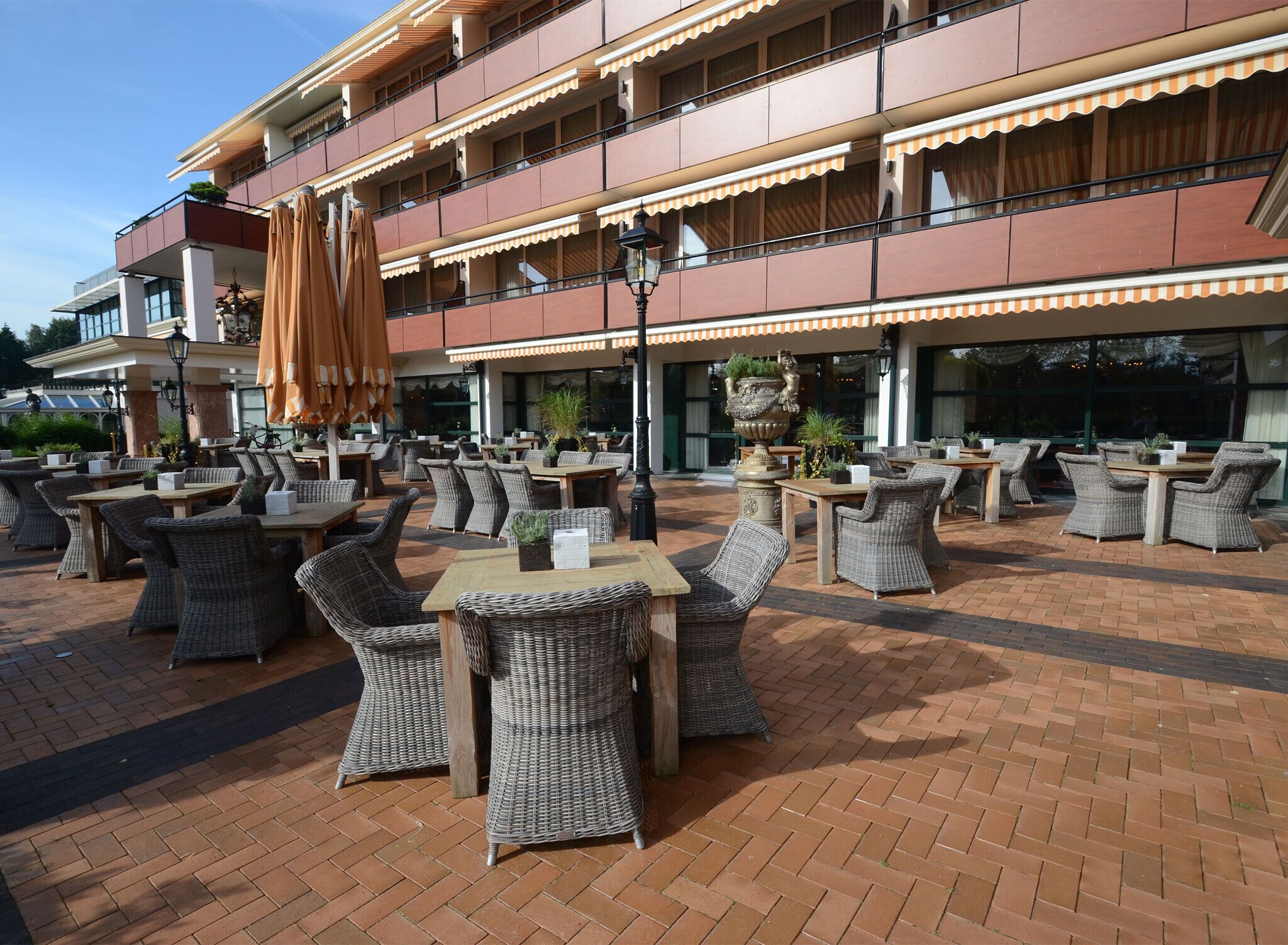 An outdoor seating area with wicker furniture and umbrellas, a brick floor, and a building with multiple balconies.
