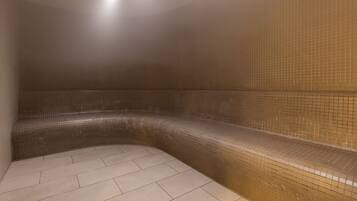 A steam room with tiled walls and floor, a bench, and a light fixture.