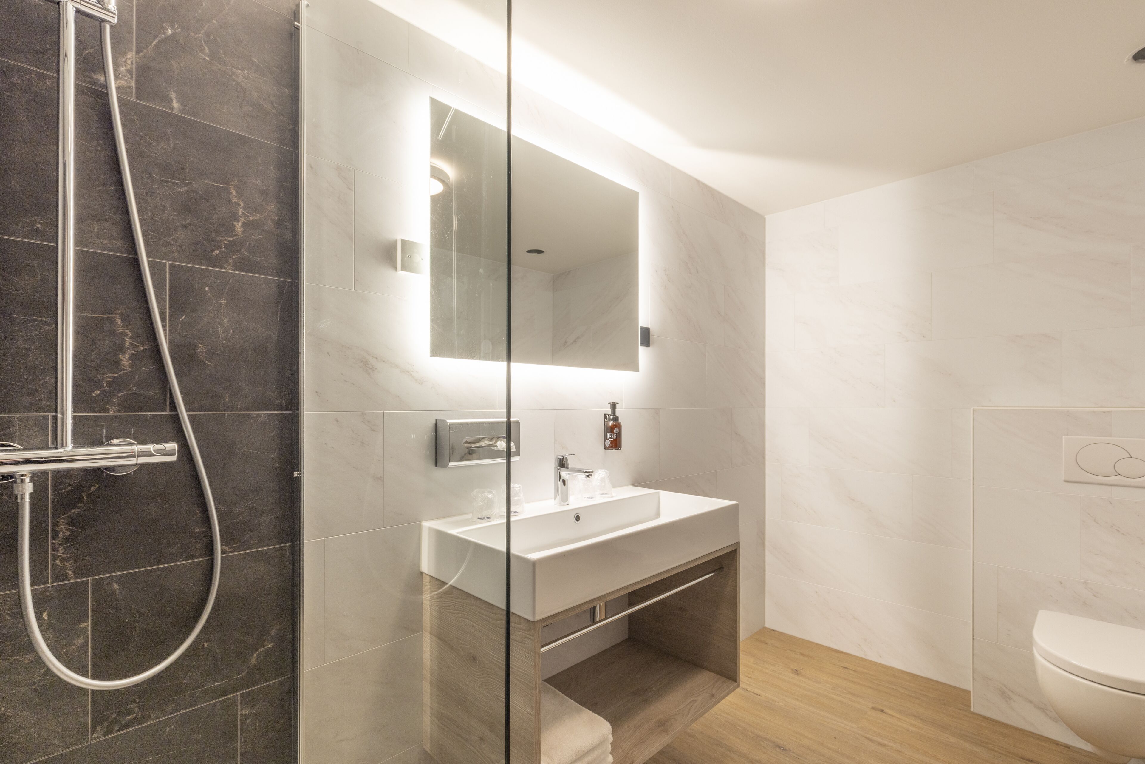 Un baño moderno con ducha de vidrio, lavamanos blanco y tocador de madera.