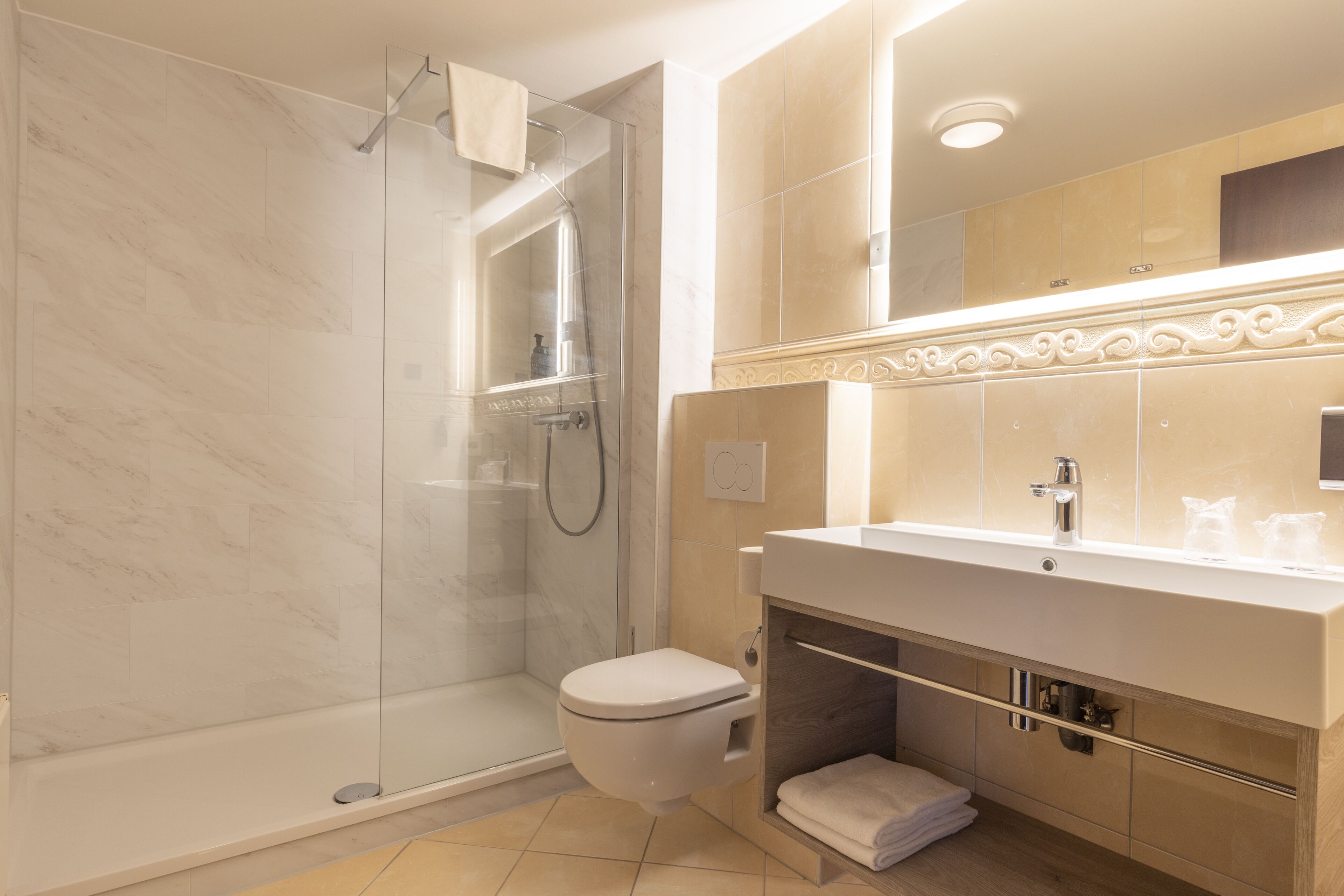 Un baño moderno con ducha envuelta en vidrio, inodoro blanco y tocador con espejo y lavabo.