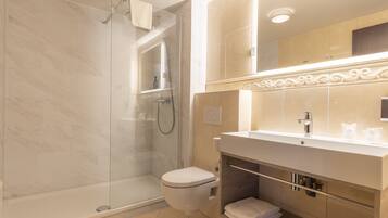 Un baño moderno con ducha envuelta en vidrio, inodoro blanco y tocador con espejo y lavabo.