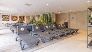 Een moderne wachtruimte met grijze loungestoelen, een receptiebalie en een muur met een natuurlandschap.