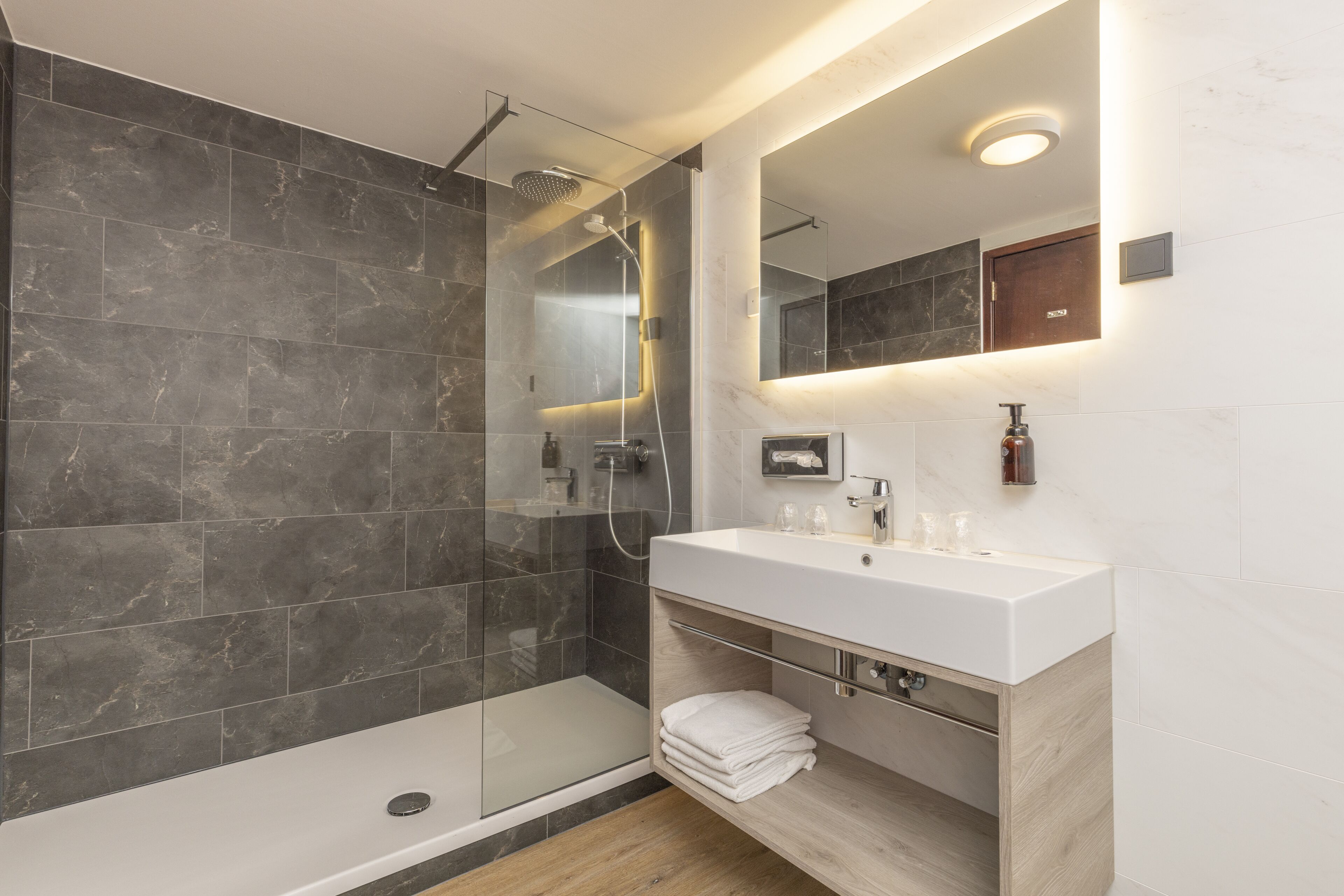 Ein modernes Badezimmer mit einer Glaskabine, einem weißen Waschbecken und einer Holzwaschkommode.