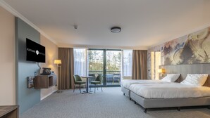 Een hotelkamer met een groot bed, een bureau met stoel, een televisie en uitzicht op het omliggende landschap.
