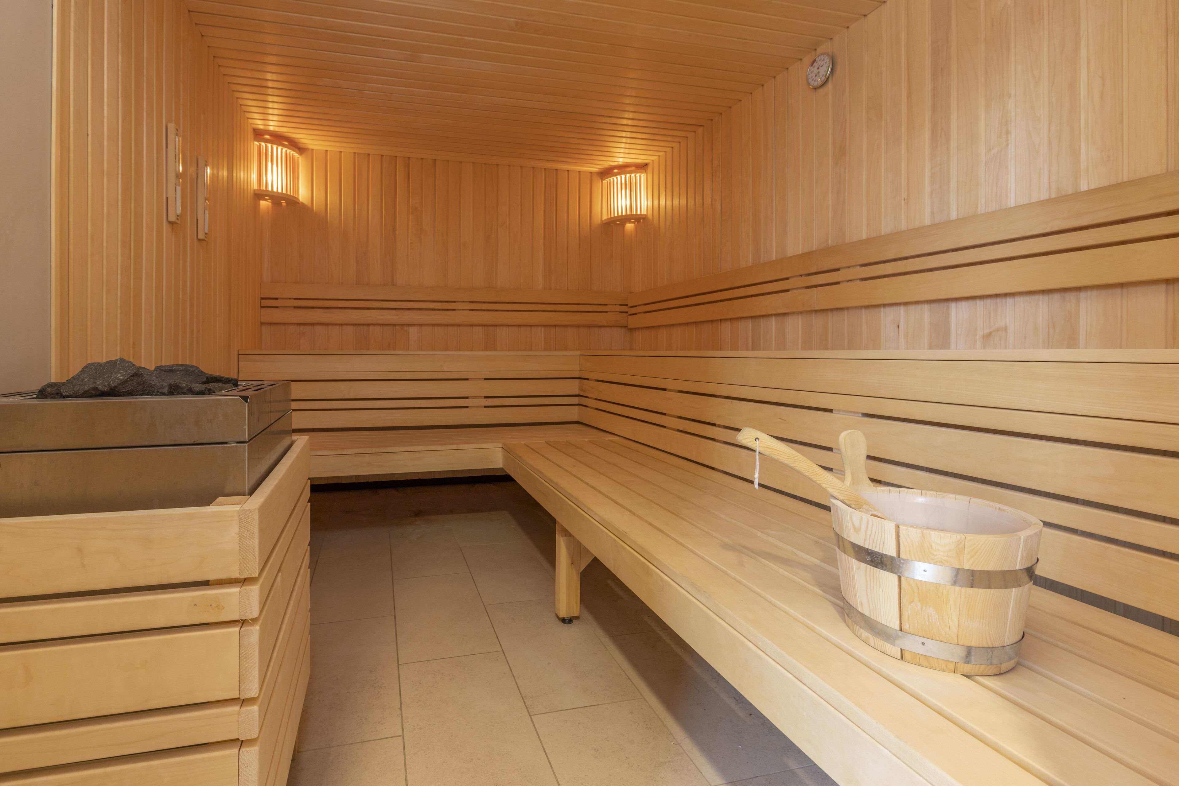 A sauna with wooden benches, a sauna heater, and a bucket.