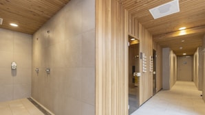 Een gang met houten lambrisering en betegelde vloer, die leidt naar een badkamer met douche en toilet.