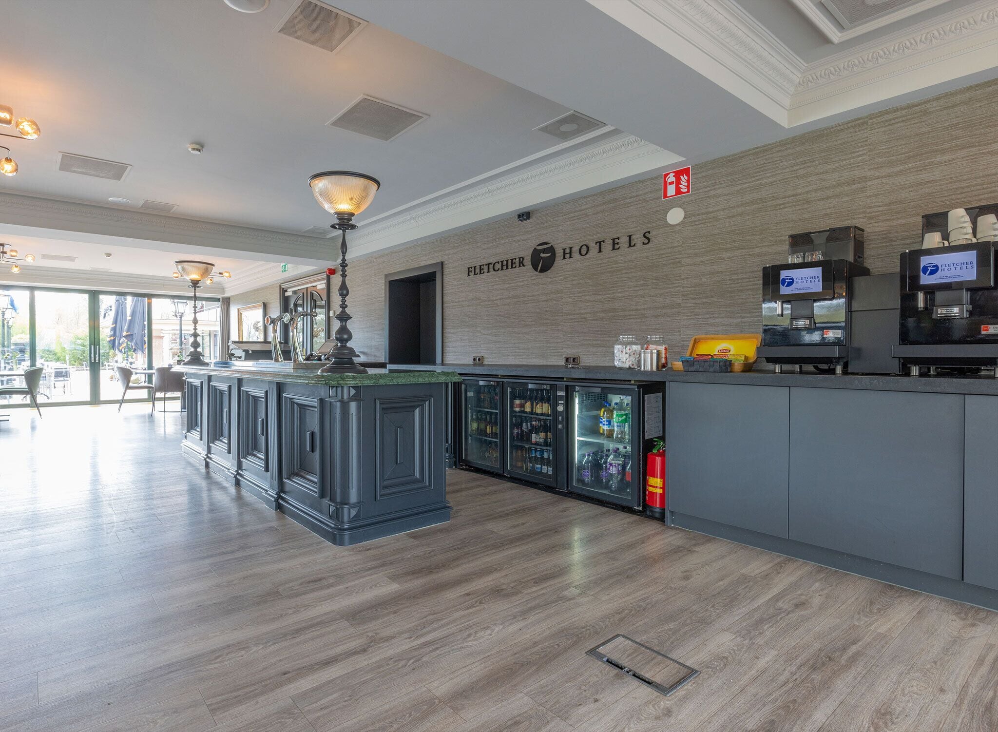 A hotel lobby with a reception desk, a coffee machine, and a fire extinguisher.